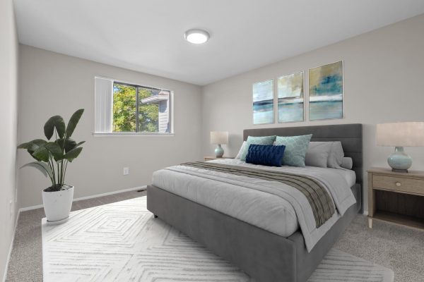 Modern bedroom with gray bed, abstract wall art, potted plant, and natural light from window. Cozy and stylish decor.