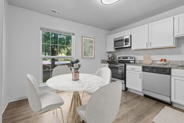 Modern kitchen with white cabinets, stainless steel appliances, and a marble dining table near a large window.